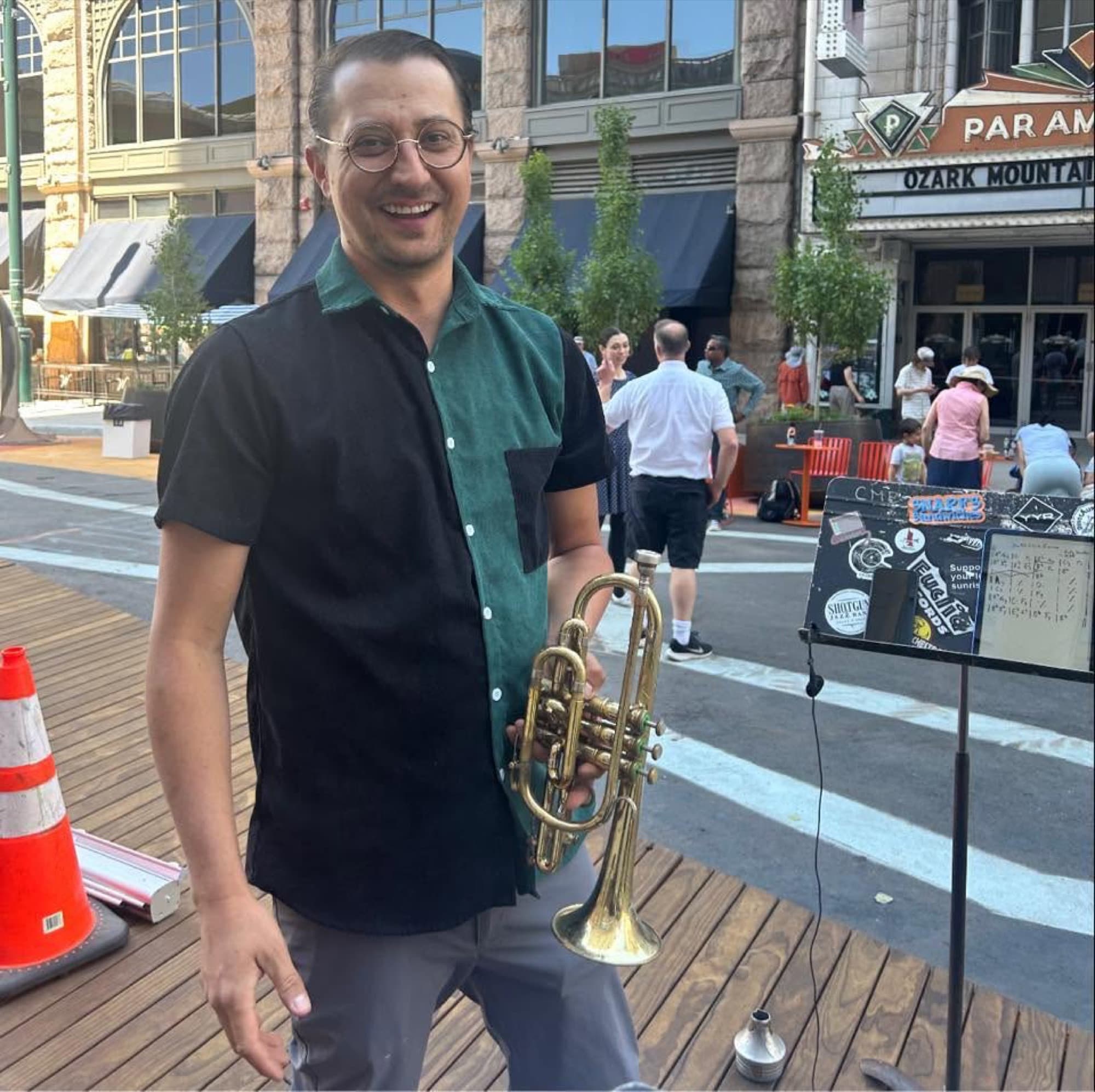 Reid Poole smiling and holding a trumpet downtown